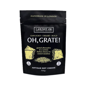 Packaging of 'I am Nut OK' vegan pizza topping set, with the product name 'Oh, Grate!' prominently displayed, indicating a grated cheese alternative. The package is black with yellow text and graphics.