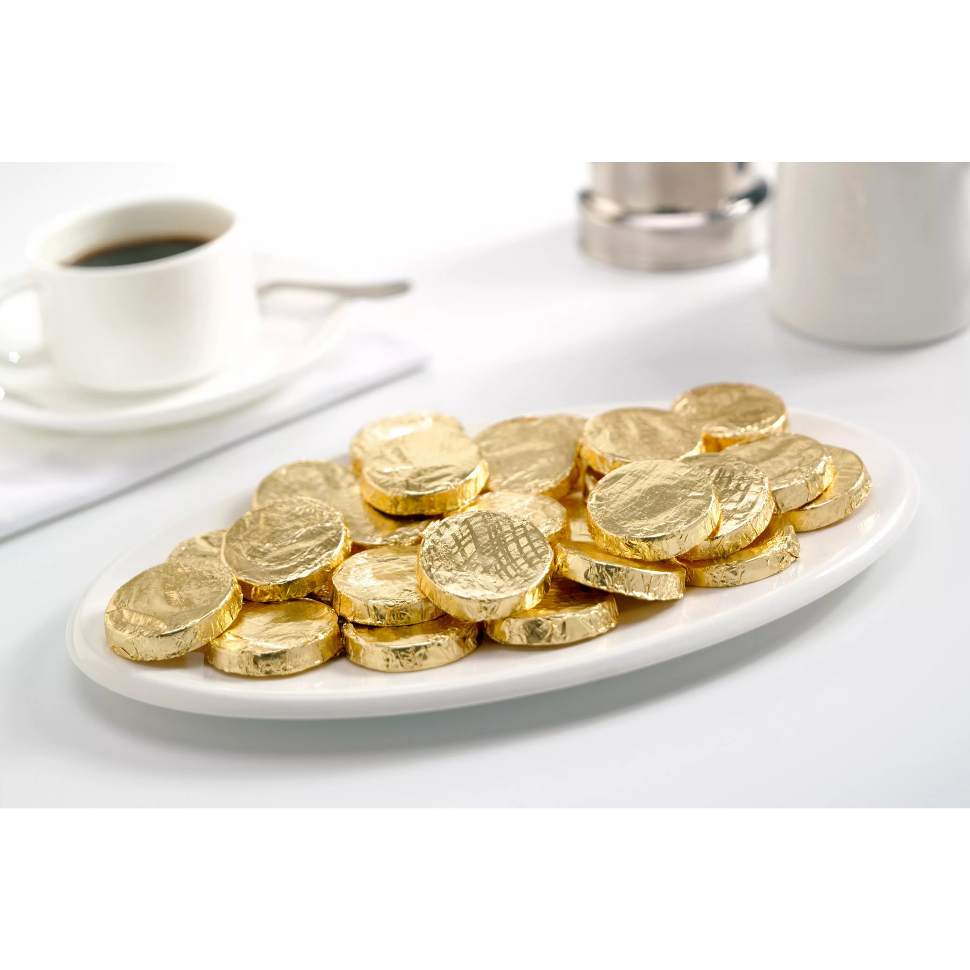 Gold-wrapped chocolates on a white plate with a cup of coffee in the background